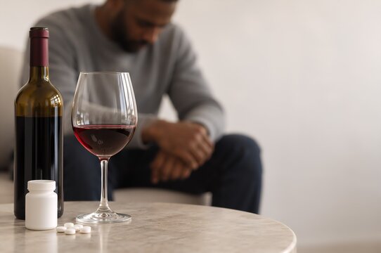 Wine, medication bottle and pills beside seated person. Alcoholism and antidepressant treatment concept. Addiction recovery, mental health and substance use care.