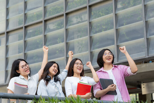 Four female university students celebrate outside a modern campus building with raised hands and smiles, representing teamwork, friendship, confidence, unity, student life, and academic success.