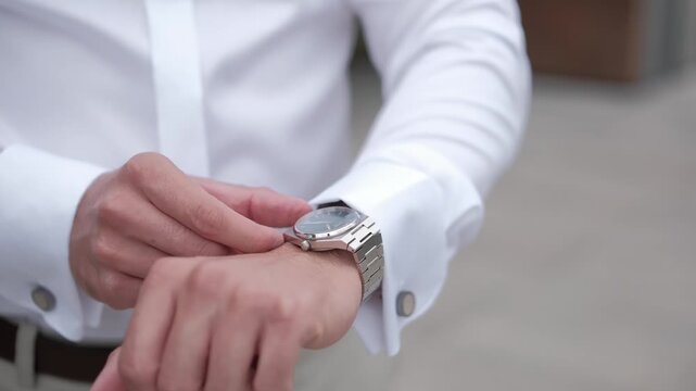 Close up of a man in a white shirt adjusting his cufflinks while getting dressed