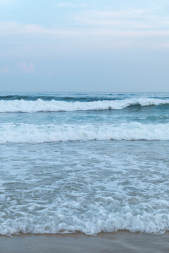 Gentle ocean waves roll onto the sandy beach under pale blue sky