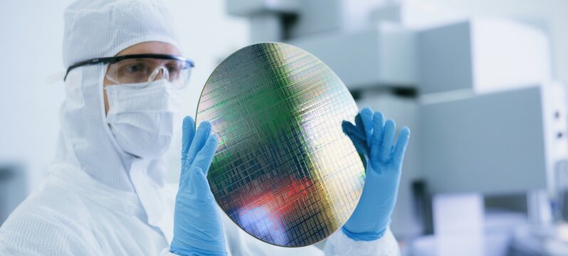 Cleanroom worker holding a silicon wafer during semiconductor inspection