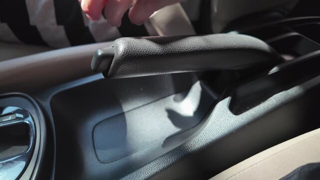 Close-up of hand pulling handbrake and unbuckling seatbelt inside car. Concept of parking vehicle, road safety, ending trip, and automotive interior details.