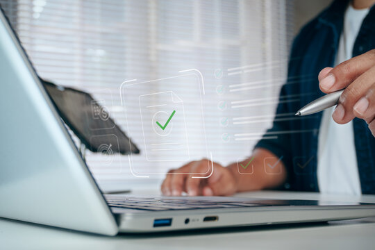 Businessman holding pen and typing on laptop with digital document check mark icon and online checklist interface overlay, concept of paperless office, approval, and management.
