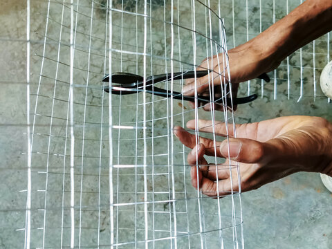 Worker hands cutting wire mesh with pliers on concrete floor. Hands using wire cutter pliers to cut roll of silver galvanized steel wire mesh fencing. DIY construction, craftsmanship, and manual labor