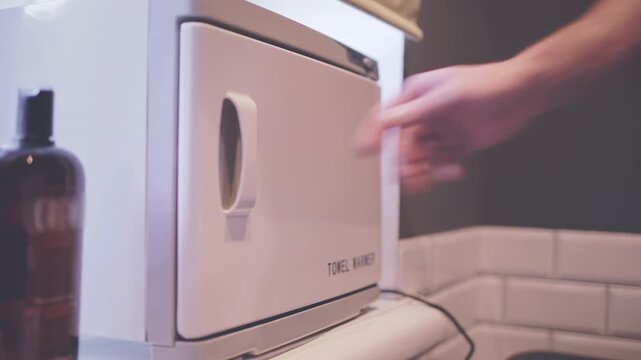 Hot towel warmer closeup. Barber hand opening door taking white cloth salon.