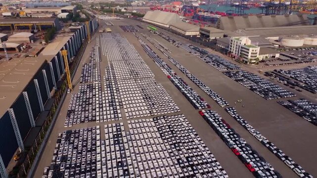 High angle aerial drone perspective over massive outdoor parking lot filled with brand new exported vehicles