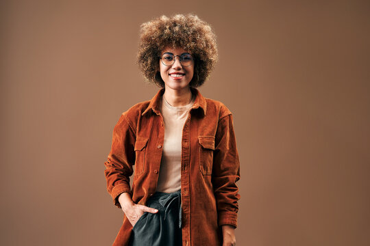 Smiling woman in rust jacket against brown background.