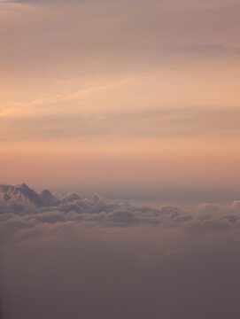 Pastel sunset sky above a sea of clouds seen from an airplane
