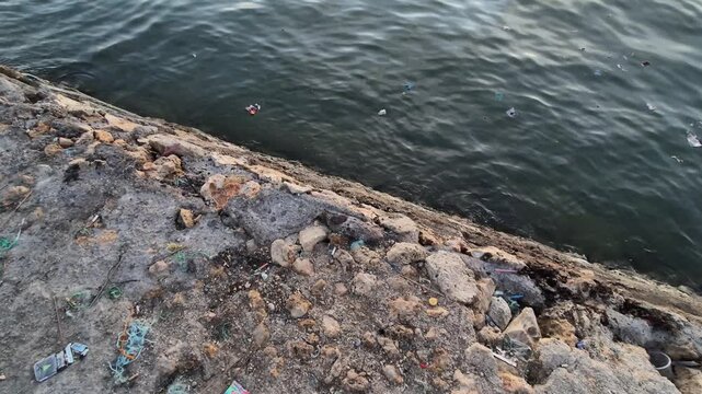 High angle view of plastic waste and garbage on a rocky shore and sea water at the harbor
