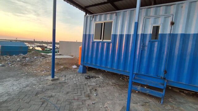 Blue and white shipping container office building on a paved yard at the harbor during sunset