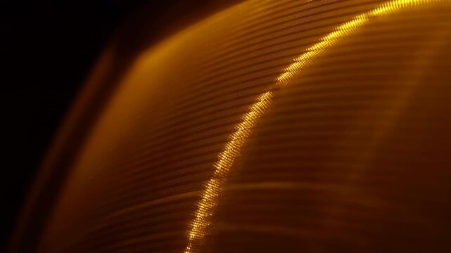 Golden ridged surface shimmers with subtle changes in bright highlights along curved parallel lines, filling close-up abstract composition with amber tones against dark background