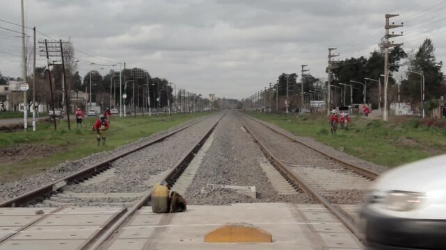 Suburban Railway Level Crossing with Workers Mowing Grass and Passing Traffic in Buenos Aires Province, Argentina