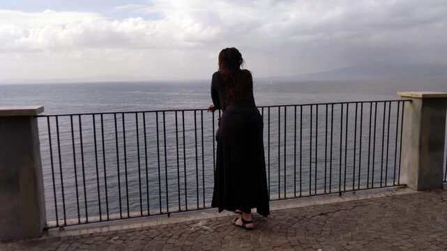 Young Woman in Black Dress Standing on Balcony Overlooking Sea at Sunset in Sorrento