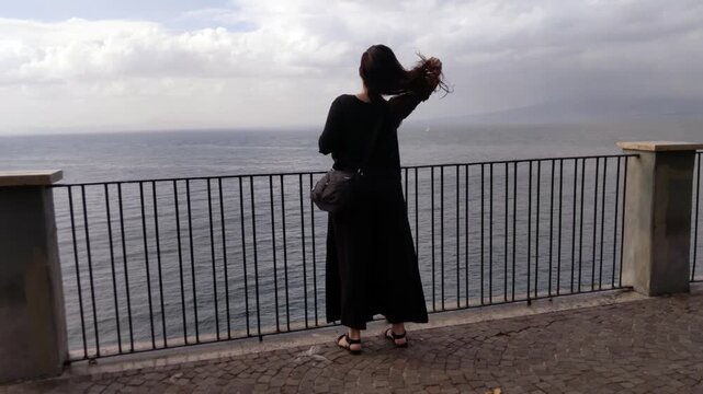 Young Woman Adjusting Her Hair on Cliffside Balcony Overlooking Sea in Sorrento 