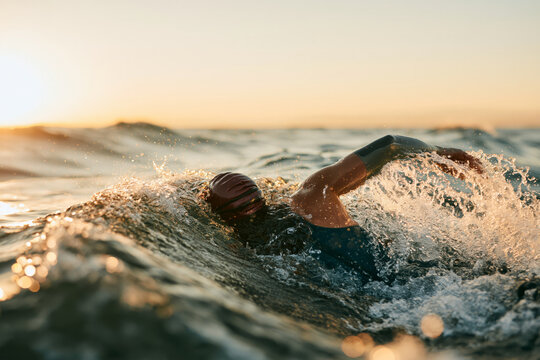 Open water swimming athlete ocean sunrise splash, freestyle stroke in waves, energetic focus