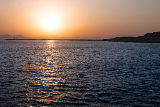 Scenic sunset over sea or ocean with mountain range on horizon