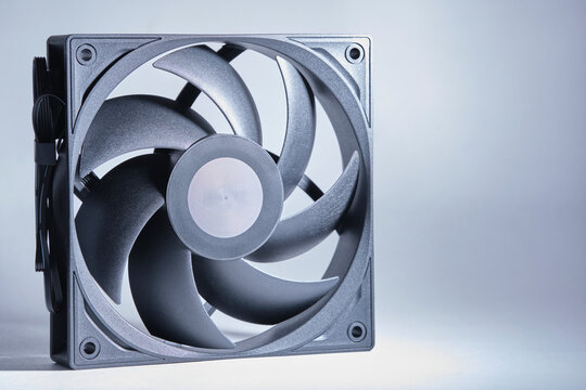 Modern black computer PC cooling fan with curved blades isolated on light neutral studio background.