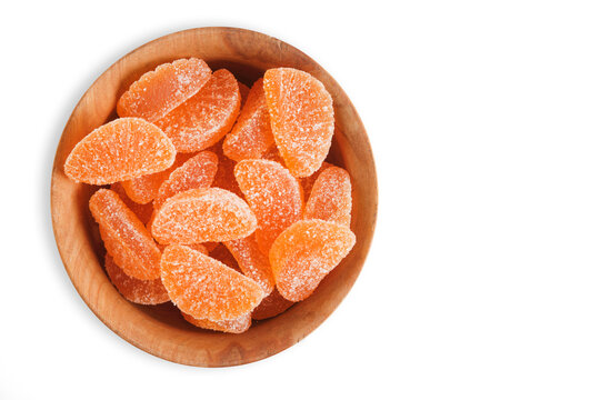 Top view wooden bowl filled with orange citrus marmalade candies on white background with space.
