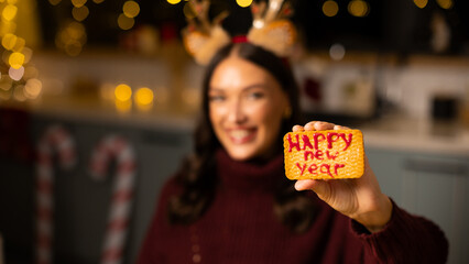 Woman wearing reindeer antlers smiling showing festive cookie with Merry Christmas phrase, selective focus, panorama © Home-stock