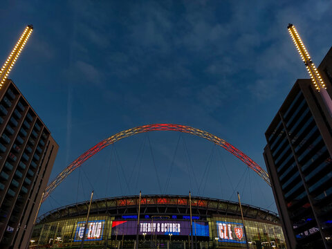 Sports and Architecture: Illuminated Wembley Arch Framed by Modern Buildings at Twilight During Matchday at Wembley Stadium