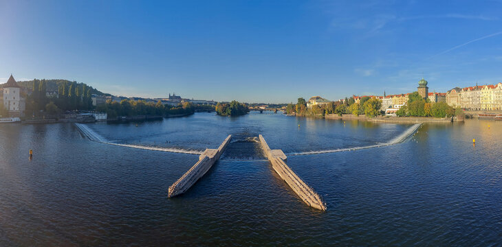 Travel and History: Panoramic View of Vltava River Weir and Wooden Icebreakers with Prague Castle and &Scaron;&iacute;tkov Water Tower on Horizon in Prague