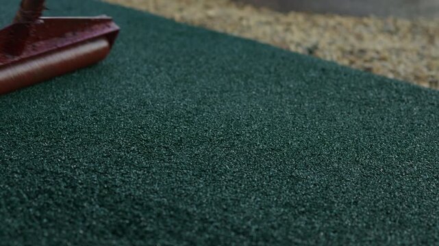 Worker leveling rubber crumb flooring with smoothing tool during installation