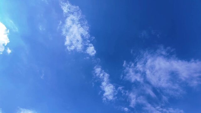 Timelapse of white wispy clouds drifting across a deep blue sky, sunlight glowing on the left side, nature and weather concept, bright daytime scene with no people or objects