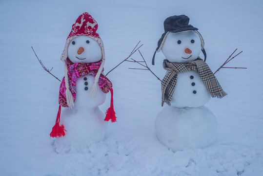 Snowman and two snowmen friends. Snowman couple in winter snow. Cute snowman with knitted scarf. Smiling snowman on snowfield. Snow man concept.