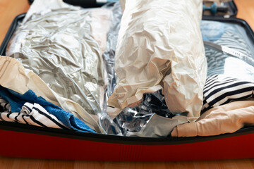 open suitcase packed with clothes and vacuum storage bags top view, both halves filled with folded garments on a wooden floor concept of travel, vacation, packing © Lana Pietukhova