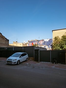 Kyiv, Ukraine - Aug 29, 2026: A white Ford C-Max compact car is parked on Alla Tarasova Street, adjacent to a fenced-off courtyard slated for development within a UNESCO buffer zone, with urban