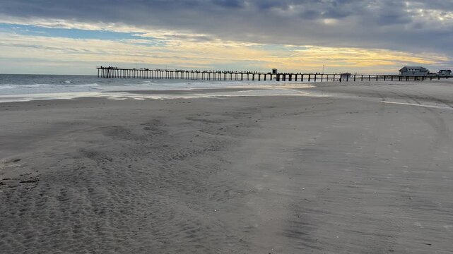Tilt up view from a big flat sandy beach exposing a lobg fishing pier and then a dramatic cloudy sky
