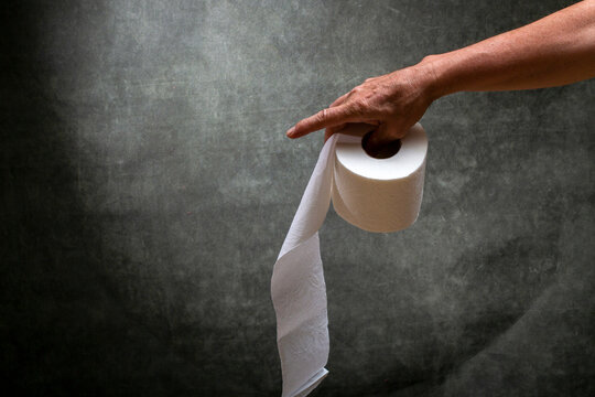 Man's right hand holding a roll of white toilet paper
