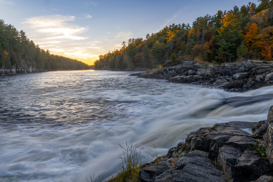 Recolett Falls cascades over rocks in French River Provincial Park, Ontario, at sunset, with autumn foliage enhancing the serene landscape.