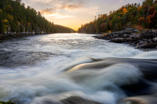 Dynamic view of Recolett Falls cascading over rocks at sunset in French River Provincial Park, Ontario, surrounded by vibrant autumn foliage.