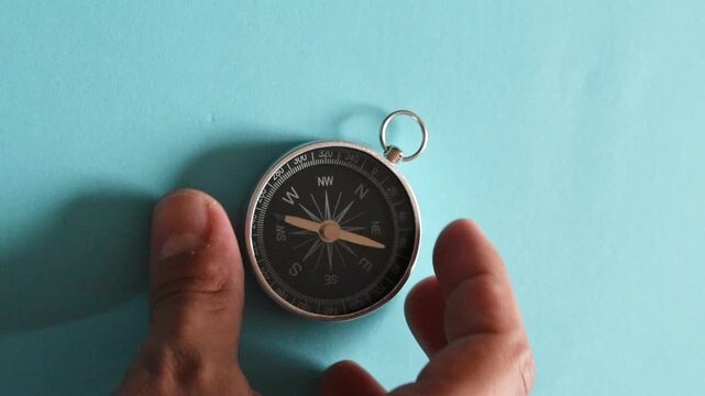 Hand placing a magnetic compass on blue background, navigation and direction concept