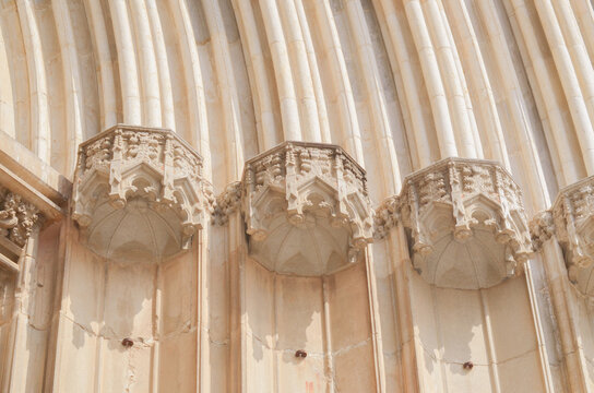 Ancient gothic cathedral portal with carved stone niches and columns. Close up of medieval church architectural details, ornate canopies for statues, and historic sandstone facade