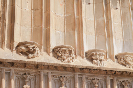 Gothic carved stone consoles and pilasters on an ancient cathedral facade. Close up of medieval architectural details, gargoyle sculpture, angels, and historic sandstone church wall ornament