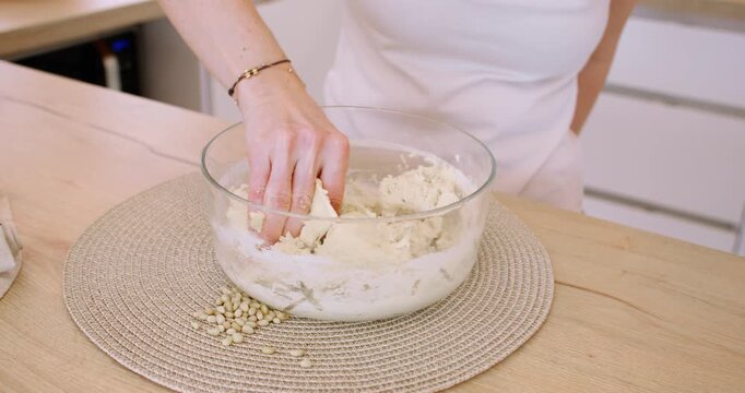 Homemade food process. Baking treat. Woman chef hand kneading dough in bowl preparing tasty pastry at wooden table with pine nuts.