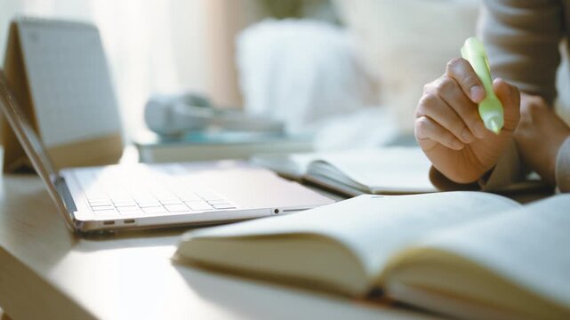 Text highlighting follows a highlighter across an open book beside a laptop, with the highlighter marking lines on the page as the close view records text highlighting during quiet home revision.