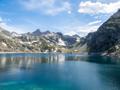 Alpine Mountain Lake with Snow Patches - Serene high-altitude lake reflecting rugged mountain peaks with lingering snow under a bright blue summer sky.