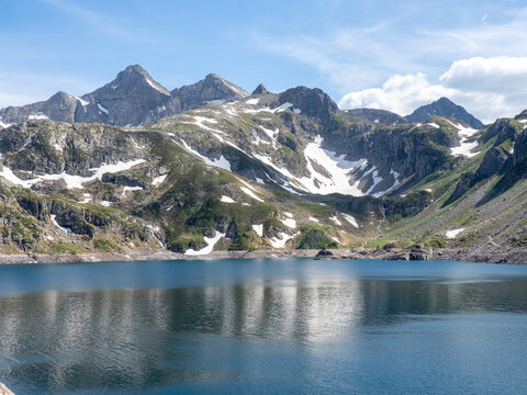 Alpine Mountain Lake with Snow Patches - Serene high-altitude lake reflecting rugged mountain peaks with lingering snow under a bright blue summer sky.
