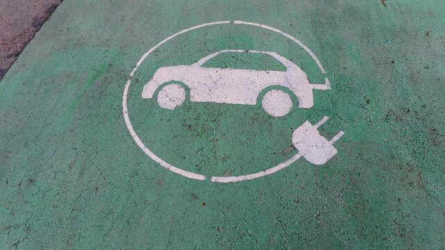 Electric vehicle charging station sign painted on green asphalt parking lot