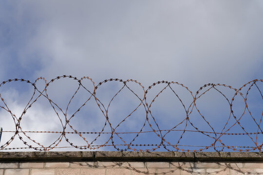 Razor wire security barrier on prison wall against sky