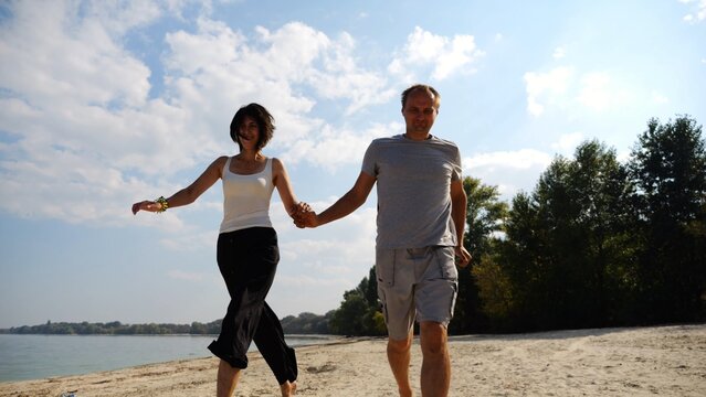 Romantic couple holding hands of each other and jogging at coastal. Happy pair running along seashore at sunny day. Lovers spending time together at resort. Concept of summer vacation or holiday