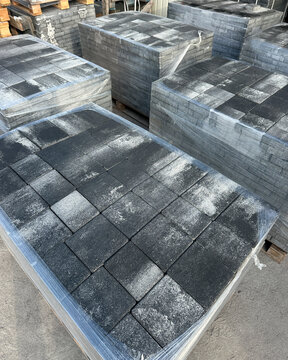 Wrapped pallet of dark grey concrete paving slabs outdoors