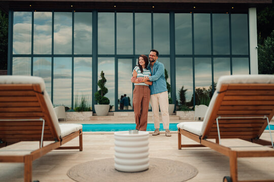 Happy couple embracing by luxury villa pool, enjoying romantic vacation and modern lifestyle outdoors