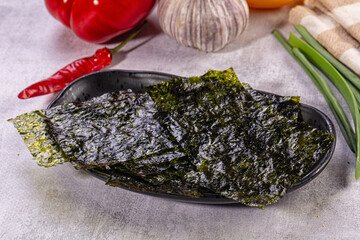 Grey stone surface with roasted nori seaweed sheets on black plate, Asian snack © Andrei Starostin