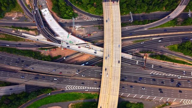 Highway intersection and cloverleaf interchange, New Jersey. Complex network of asphalt roads, overpasses, moving cars and surrounding green trees from above.
