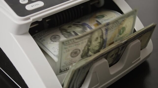 Money counting machine processing dollar bills in motion. Counting machine working in bank. Banking system processing currency. Counting money in motion. Counting dollar notes in a banking machine.