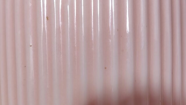 Vertical ribbed pattern on a pale pink glossy surface, close-up texture background, pastel
